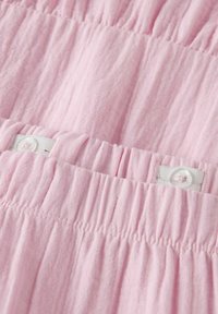 Heller pinker Stoff mit einer zerknitterten Textur, der geraffte Bereiche und einen weißen Knopfverschluss für eine verstellbare Passform aufweist.