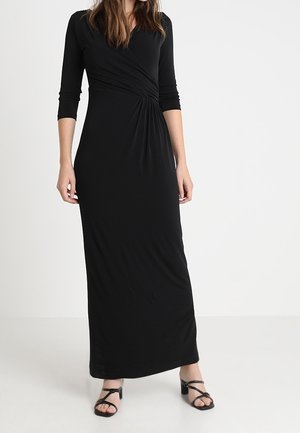 Schwarzes, langärmeliges Maxikleid mit gerafftem Design an der Taille. Hergestellt aus weichem, dehnbarem Stoff, kombiniert mit schwarzen, Riemchensandalen.