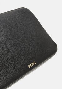 Črn usnjen denarnica z teksturirano površino, ki ima zlat logotip "BOSS" na eni strani, pravokotne oblike in zaobljenimi koti.