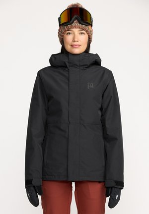 Veste imperméable noire avec un col montant, fermeture éclair à l'avant et logo, accompagnée de gants noirs et d'un bonnet tricoté avec un pompon dans des couleurs atténuées.