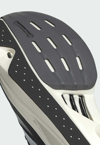 Schuhsohle mit einem grauen Gummibereich, der Rillen und Perforationen aufweist, weißen Akzenten und einem strukturierten schwarzen Bereich für Halt.