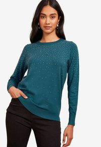 Türkooker, pikkade varrukatega, ümar kaelus ja sädelevate rhinestones'iga kaunistused. Kandmiseks mustad püksid, millel on mugav istuvus.