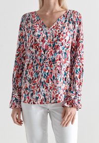 Blusa floreale astratta con scollatura a V, maniche lunghe e dettagli di polsini arricciati. I colori includono rosa, rosso, blu e bianco su uno sfondo chiaro.