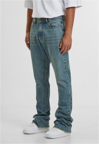 Šviesiai mėlynos džinsinės kelnės su tiesiu kirpimu, penkiomis kišenėmis ir matomomis siuvimo detalėmis; derinamos su baltomis sportinėmis batų.