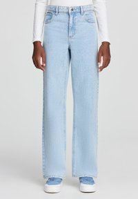 Jasnoniebieskie dżinsy z wysokim stanem, o szerokim kroju nogawki i pięcioma kieszeniami. Zawierają zapięcie na guzik oraz widoczne szwy.