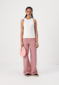Weißes ärmelloses Tanktop, rot-gestreifte, weit ausgestellte Hose und eine rosa Handtasche. Die Hose hat einen strukturierten Stoff, und die Schuhe sind schwarz mit einer hellen Sohle.