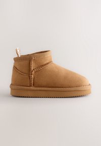 Bottine en daim marron clair avec coutures cousues, languette en tissu et semelle en caoutchouc plate sur fond neutre.