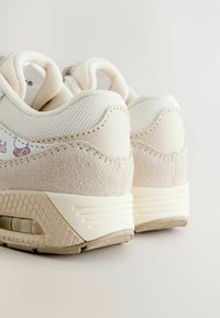 Kermavaale sneakerit, joissa on tekstuuri beige nubukipohja, verkkomateriaali yläosa ja kuviolliset yksityiskohdat. Ominaisuuksia näkyvä ilmapallo pohjassa.