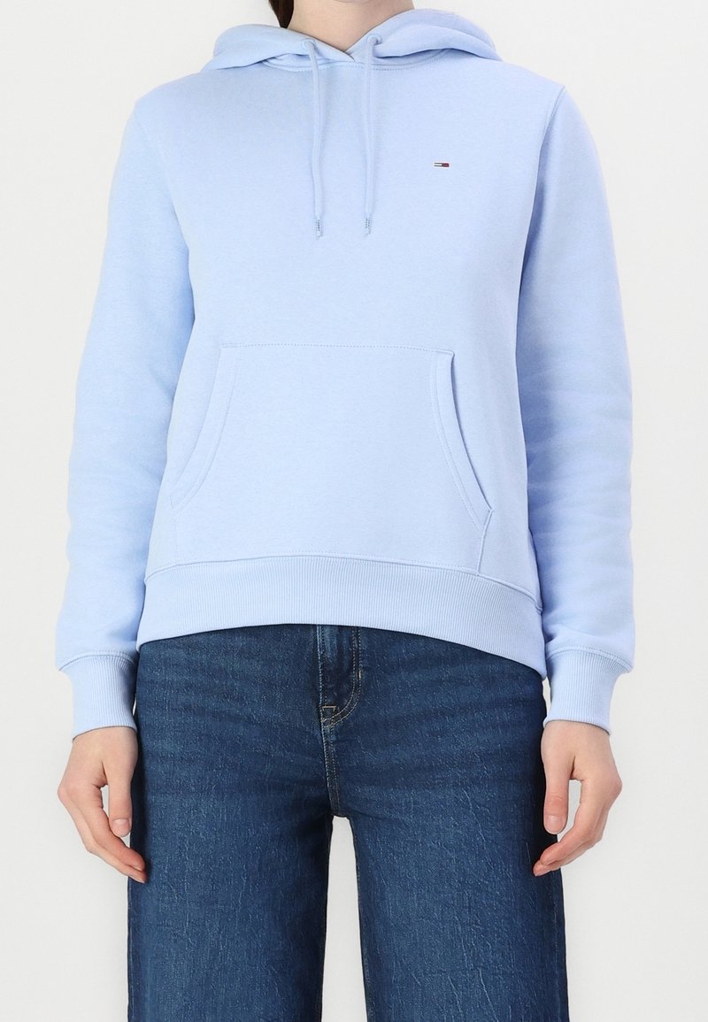 Light blue hoodie made of soft fabric with a front pocket, drawstring hood, and ribbed cuffs and hem. Small logo detail on the chest.