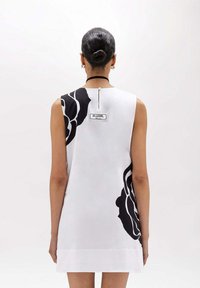 Abito bianco senza maniche con un design floreale nero su un lato. Presenta uno spacco sul retro e un'etichetta con la scritta "BLUGIRL". Tessuto morbido.