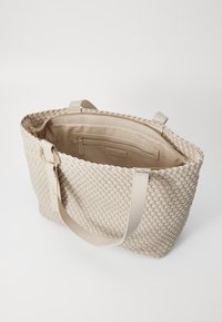 Sac fourre-tout tissé beige avec double poignées, fermeture zippée en haut et poches intérieures. Texture lisse et forme structurée, idéal pour un usage quotidien.
