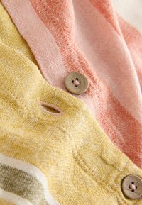 Tissu multicolore présentant des rayures douces et texturées en pêche et jaune, avec un bouton beige à l'intersection et des détails de couture visibles.