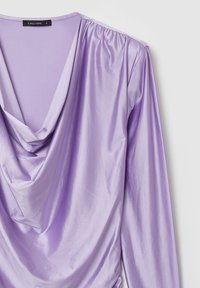 Top lungo a maniche drappeggiate in seta satinata di un delicato colore lavanda, con scollo a cowl e dettagli arricciati sulle spalle. Etichetta del marchio visibile.