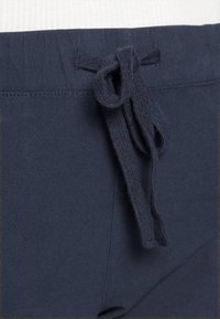 Navy blauwe sweatpants met een textuur in de tailleband en een gestrikte koord. Het materiaal lijkt zacht met een gladde afwerking en subtiele stikdetails.