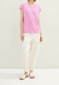 Rosa kortärmad t-shirt med rund halsringning i kombination med vita cargobyxor med sidofickor och beigea slip-on sandaler.