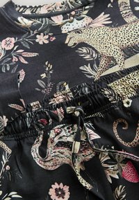 Czarny materiał z kwiatowymi i zwierzęcymi wzorami, z okrągłym dekoltem, elastyczną talią i detalem z troczkiem. Żywe, kolorowe wzory.