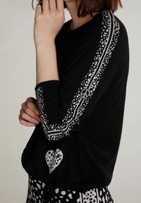 Schwarzer Strickpullover mit weißen gemusterten Streifen an den Ärmeln, vorne mit Herzmotiv, weiche Textur und lockere Passform.