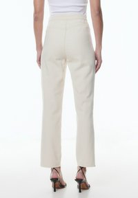 Weiße hoch taillierte Hose aus Baumwollmischung, mit geradem Beinschnitt und minimalen Nähten, kombiniert mit schwarzen Riemchen-Absätzen.