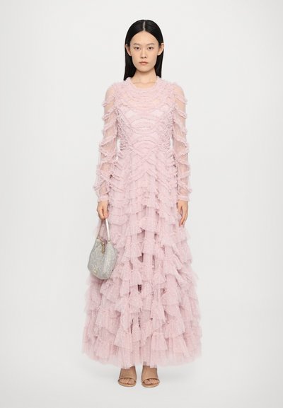 Lange roze jurk met gelaagde ruffles, sheer lange mouwen, gestructureerde stof en stippen. Vergezeld van een kleine zilveren handtas.