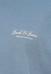 Ανοιχτό μπλε βαμβακερό μπλουζάκι με κεντημένο κρεμ κείμενο "Jack & Jones" και "ARCHIVE SELECTION" σε καλλιγραφική γραμματοσειρά. Λείο υφή.