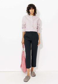 Chemise boutonnée à rayures rose clair avec une poche poitrine, associée à un pantalon noir sur mesure, des chaussures à imprimé animal à enfiler et un sac à épaule rose.