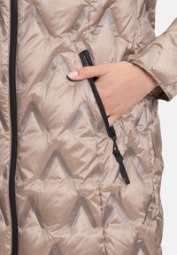 Lichtbeige gewatteerde jas met een zigzag-quiltontwerp, zwarte ritszak en een soepele satinachtige textuur.