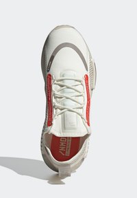 Vit sportskor med överdel i texturerad tyg, röda accenter, minimalistisk design och framträdande snörningssystem. Har en vadderad innersula.