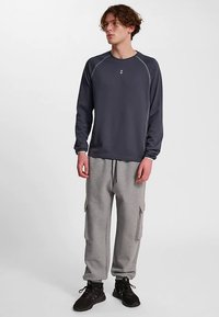 Mörkgrå långärmad sweatshirt med ljusgrå sömmar, tillsammans med ljusgrå cargo sweatpants med sidfickor och dragsko i midjan.