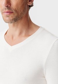 T-shirt bianca a scollo a V realizzata in morbido cotone, caratterizzata da una superficie liscia e un design aderente che valorizza il collo.