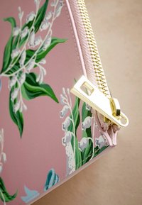 Astuccio con zip floreale rosa caratterizzato da foglie verdi e fiori bianchi. La cerniera dorata arricchisce il design. Texture esterna liscia.