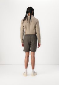 Chemise beige à manches longues et short vert olive, avec une taille élastique, présentés sur un fond blanc uni.