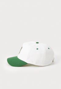 Hvit caps med grønn skjerm, dekorert med broderte detaljer og grønne øyler. Laget av bomull med en strukturert design.