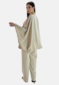 Completo beige in satin con maniche larghe e pantaloni larghi. Tessuto morbido con dettagli di design minimi e nessun motivo visibile.