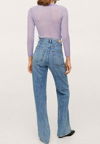 Lila pitkähihaisen puseron, jossa on teksturoitu kuvio, yhdistelmä korkea vyötäröisiin, vaaleansinisiiin, leveälahkeisiin farkkuihin, joissa on takataskut ja haalistunut pinta.