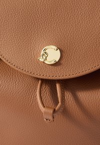 Καφέ δερμάτινη τσάντα με υφή, που διαθέτει στρογγυλό χρυσό κούμπωμα και δερμάτινη ταινία τραβήγματος, με ραμμένα άκρα και στρογγυλό καπάκι κλεισίματος.