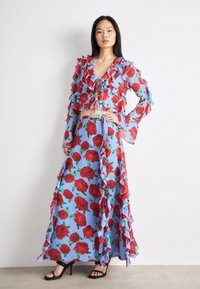 Floral two-piece outfit featuring a light blue base with red rose patterns. Ruffled details on crop top and maxi skirt with tie waist.