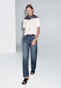 Vit kortärmad skjorta, mörkgrå scarf, mörkblå vida jeans och svarta sandaler. Enkelt mönster med en mjuk textur.