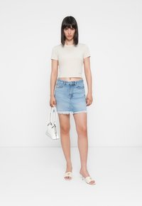 Beżowy krótki t-shirt, jasnoniebieska spódnica dżinsowa z postrzępionym dołem, białe sandały na płaskiej podeszwie i mała biała torebka. Prosty i swobodny strój.