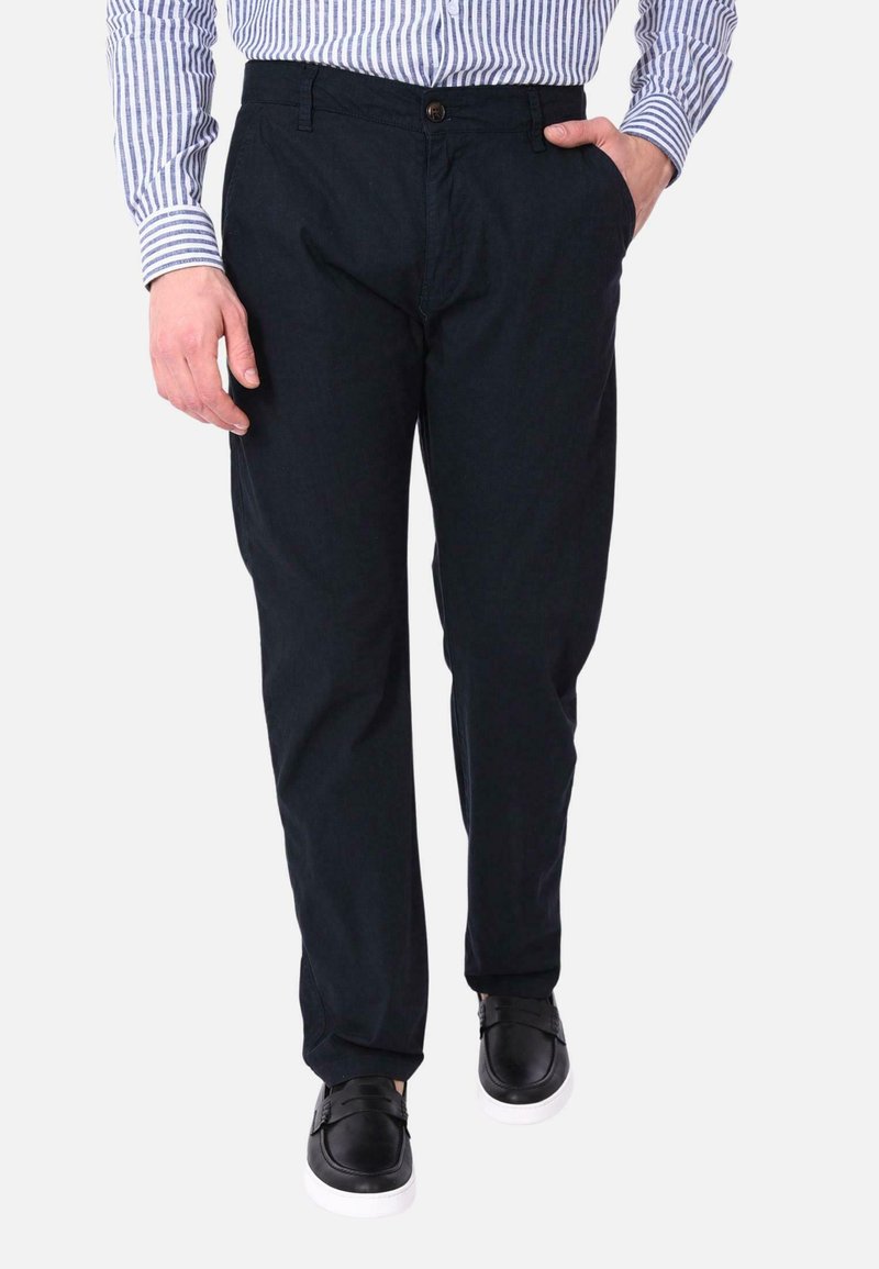 Pantaloni di cotone blu navy con taglio dritto, dotati di tasche laterali, chiusura con bottone e sneakers nere con suole bianche.