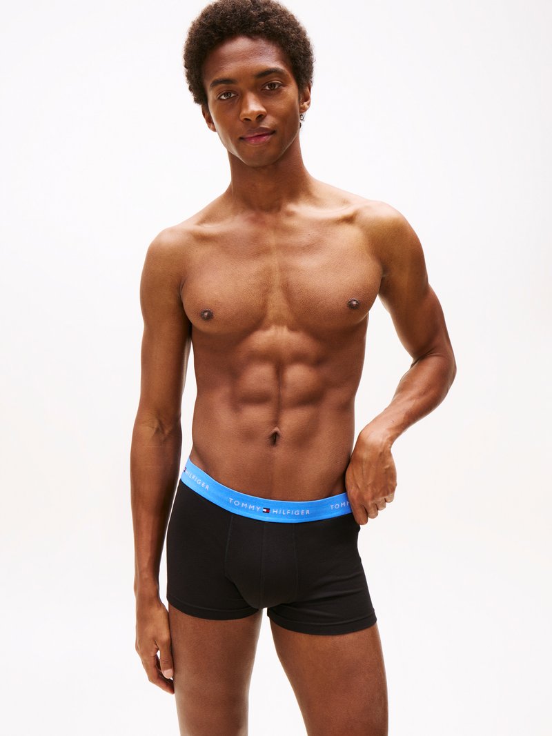 Boxer briefs neri in cotone con una vita blu decorata dal logo "Tommy Hilfiger". Il modello ha una corporatura atletica e si presenta con un'espressione neutra.