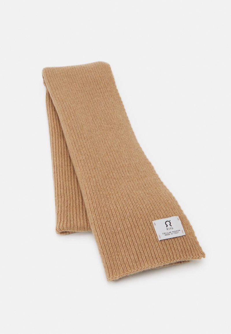 Écharpe tricotée de couleur camel chaude. Présente une texture côtelée et une petite étiquette avec un logo. Le design est rectangulaire et léger.