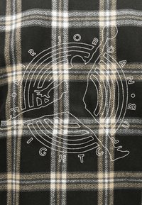 Ύφασμα σε ασπρόμαυρο, μπεζ και λευκό καρώ με λευκό περίγραμμα ενός άλτή που πηδά και κείμενο "FAIRJORDAN LIGHT UP B.O." σε κυκλικό σχέδιο.