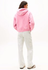 Felpa rosa cropped con cappuccio, abbinata a pantaloni cargo grigio chiaro con tasche. Il tessuto sembra morbido e la vestibilità è comoda.