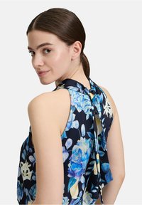 Marineblaues floral Haltertop mit blauen und gelben Blumenmustern, weichem Stoff, offener Rückseite und Bindeband am Hals.