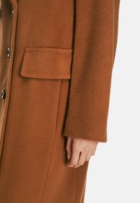 Brown wool coat featuring a textured finish, button closure, and a patch pocket on the left side of the front panel.