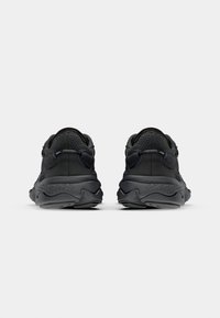 Zapatillas deportivas negras con una parte superior de malla texturizada, talón redondeado, suela de goma gruesa y dos tiradores para facilitar el uso.