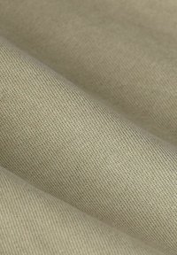 Beige katoenen stof met een gladde textuur, die een fijne weefpatroon en subtiele glans toont, in zachte plooien valt.