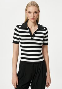 Svart och vit randig stickad polo med korta ärmar, ribbad textur, knappstängning och svart krage.