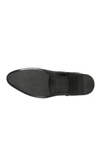 Schwarze Ledersohle mit glatter Oberfläche, abgerundetem Zehenbereich und minimalem Profil für den Grip. Subtile Texturierung in der Nähe der Ferse setzt Akzente im Design.