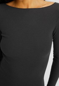 Gros plan d'une personne portant un haut ajusté, côtelé, à manches longues de couleur gris foncé avec un large décolleté.